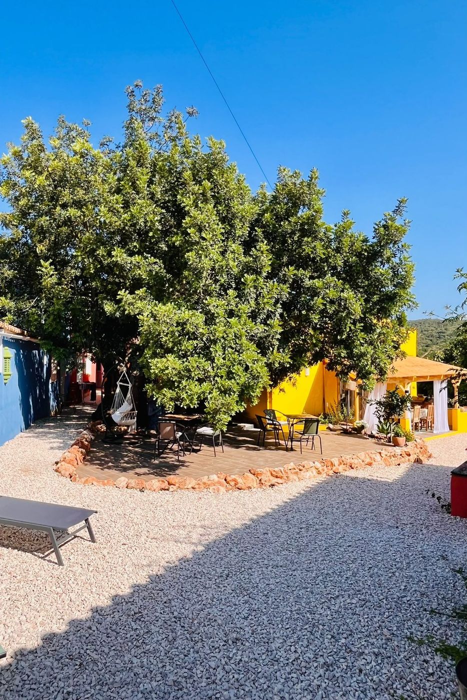 The gravel courtyard under a carob tree, hanging chair and terrace