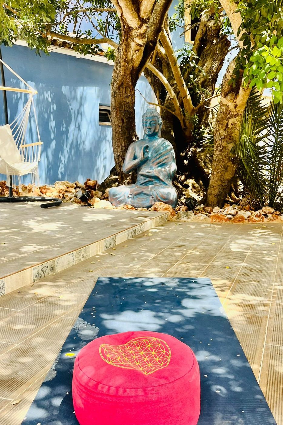 A mat and a cushion laid out in front of the buddha under the tree