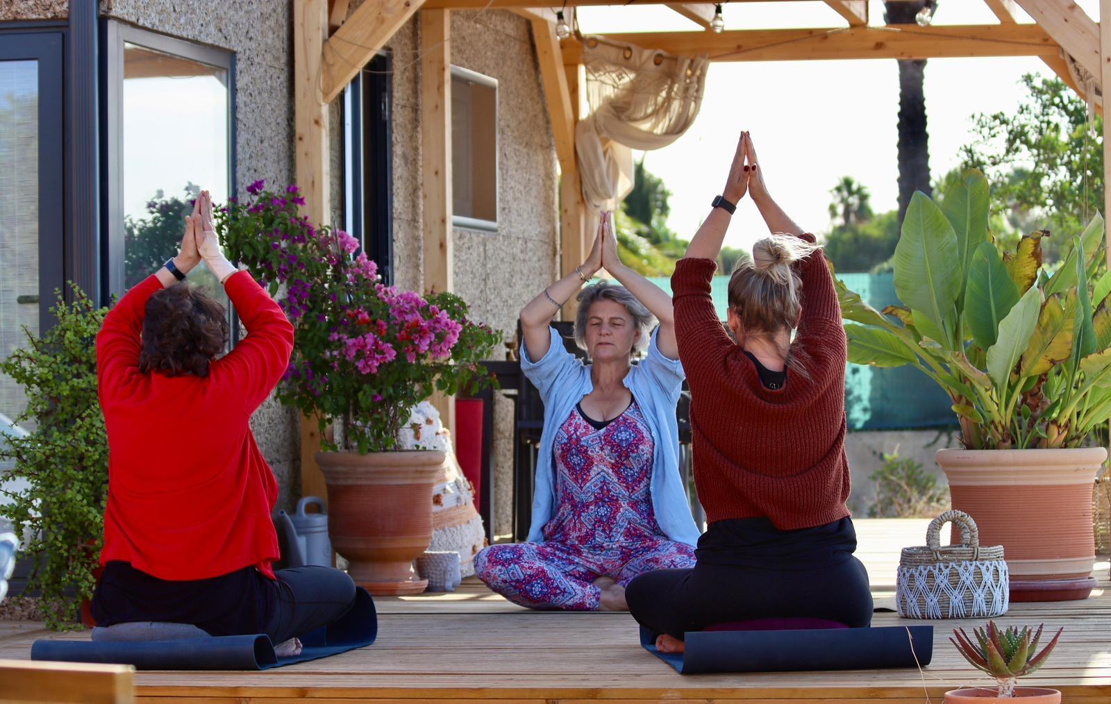 Three women in a seated yoga sequence on a wooden terrace in the morning light