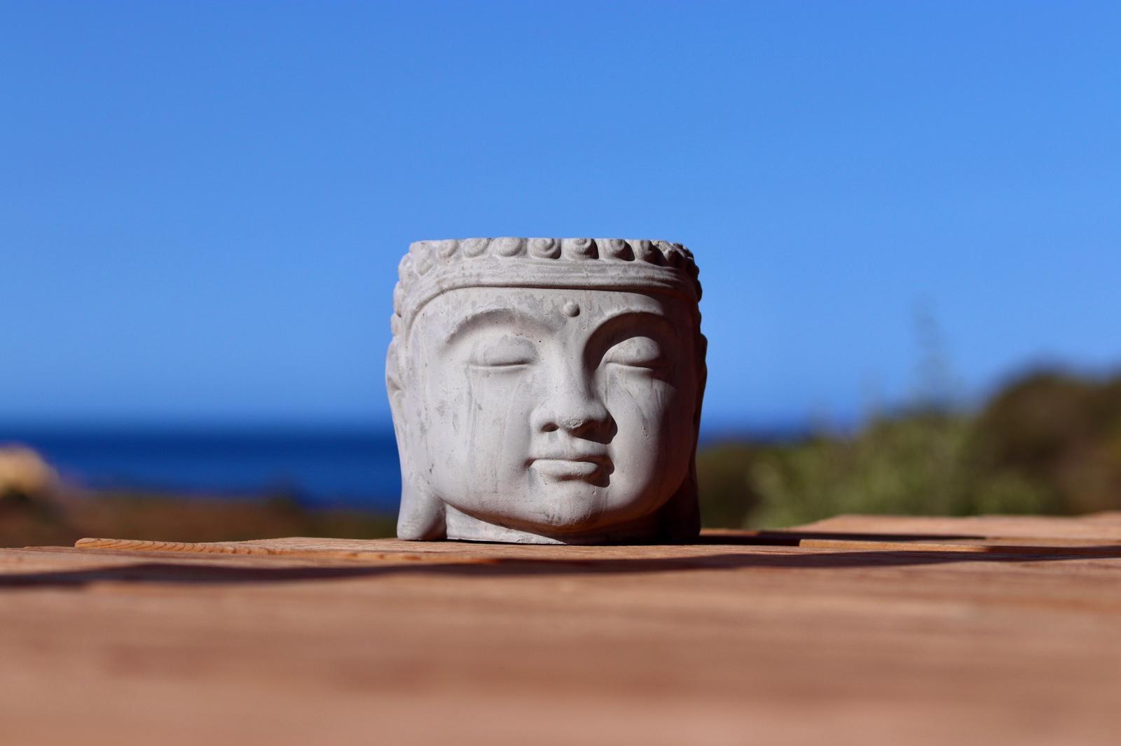 A stone buddha head on a wooden table, the sea behind it